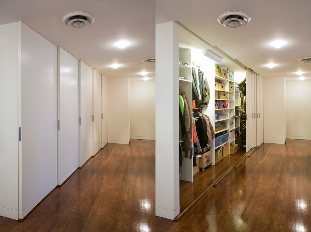 Immagine di un armadio o armadio a muro unisex minimalista di medie dimensioni con ante lisce, ante bianche, parquet scuro e pavimento marrone