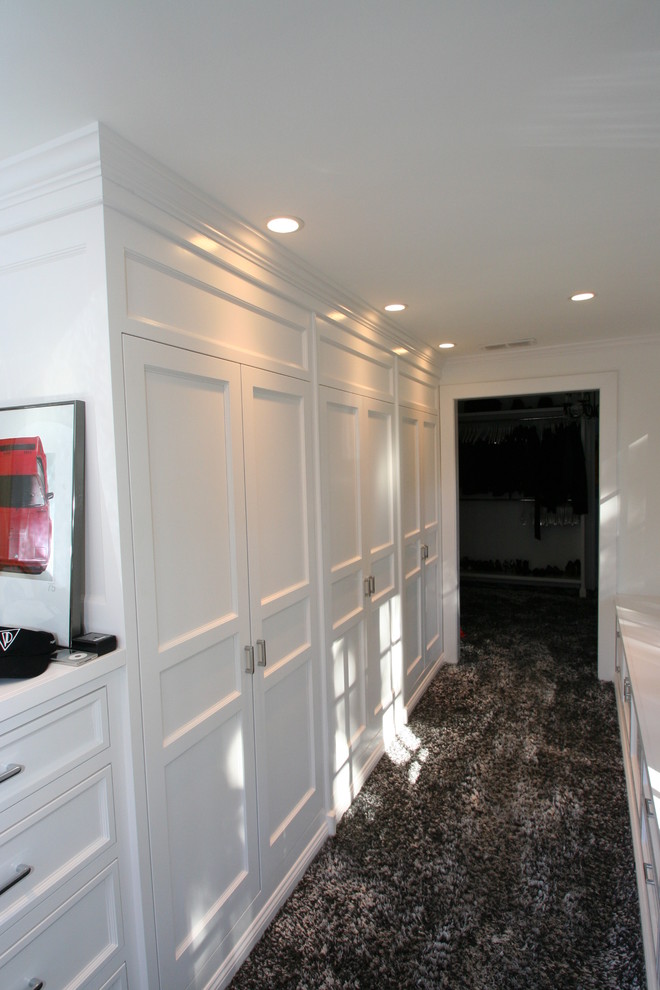 На фото: гардеробная комната унисекс в стиле неоклассика (современная классика) с фасадами с утопленной филенкой, белыми фасадами и ковровым покрытием с