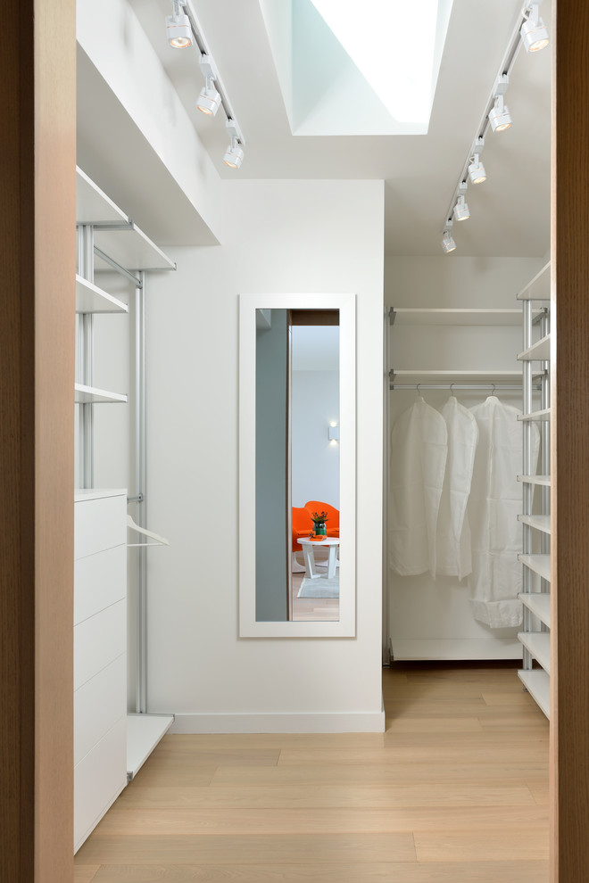 Design ideas for a contemporary gender neutral walk-in wardrobe in Toronto with flat-panel cabinets, white cabinets and light hardwood flooring.