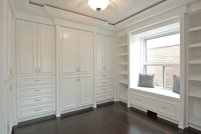 Modelo de armario vestidor unisex clásico grande con armarios con rebordes decorativos, puertas de armario blancas, suelo de madera oscura y suelo marrón