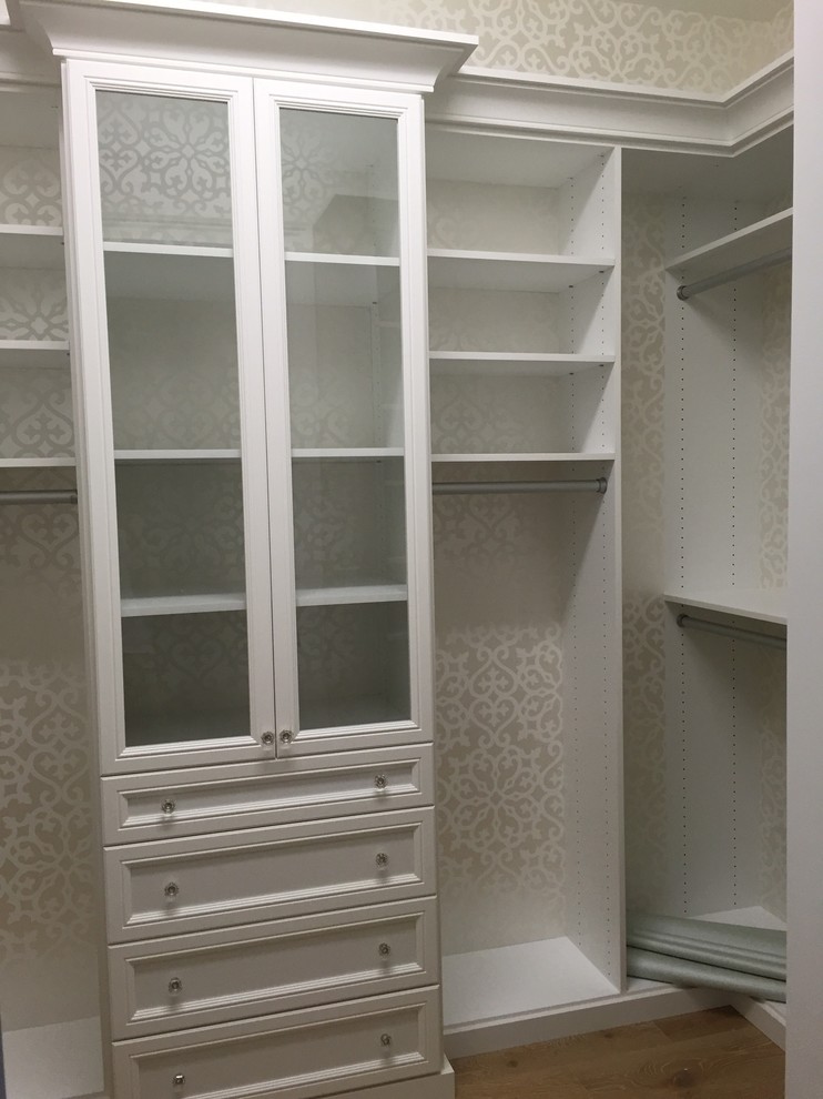 Inspiration for a coastal gender neutral walk-in wardrobe in Miami with recessed-panel cabinets, white cabinets and light hardwood flooring.