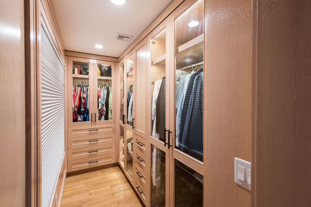 Inspiration for a small modern gender neutral walk-in wardrobe in New York with glass-front cabinets, light wood cabinets, light hardwood flooring and brown floors.