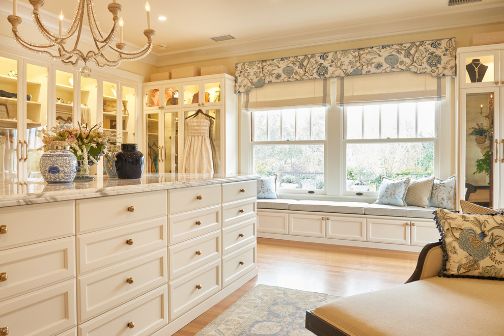 Diseño de armario vestidor de mujer clásico con armarios con paneles empotrados, puertas de armario blancas, suelo de madera en tonos medios y suelo marrón