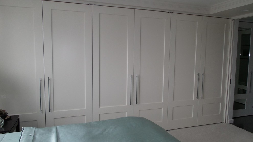 Imagen de armario y vestidor actual con armarios con paneles empotrados, puertas de armario blancas y moqueta