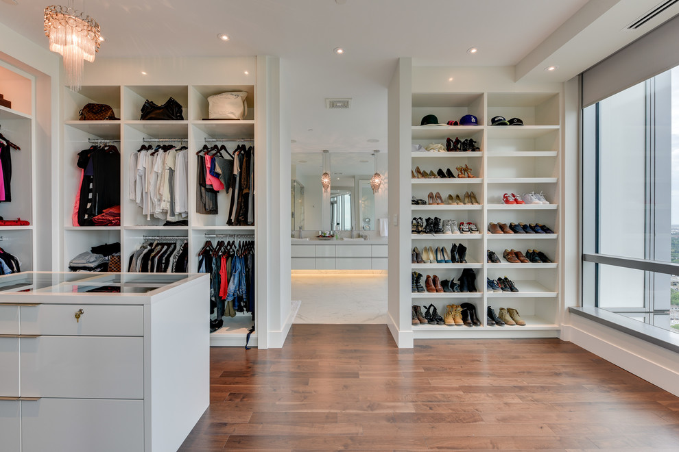 Imagen de armario vestidor unisex actual extra grande con armarios abiertos, puertas de armario blancas y suelo de madera en tonos medios