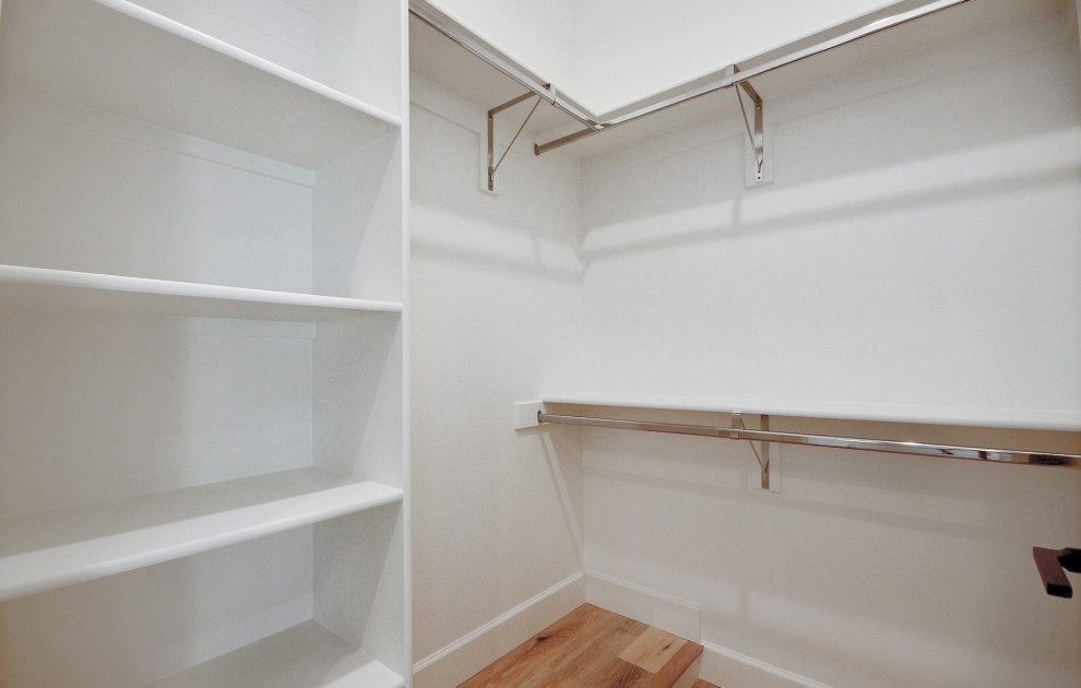 Lantlig inredning av ett stort walk-in-closet för könsneutrala, med öppna hyllor, vita skåp, ljust trägolv och beiget golv