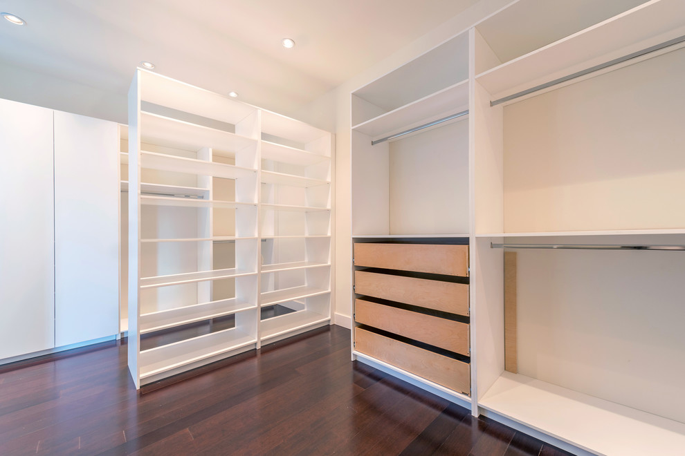 Foto de armario vestidor unisex moderno de tamaño medio con armarios con paneles lisos, puertas de armario blancas y suelo de madera oscura