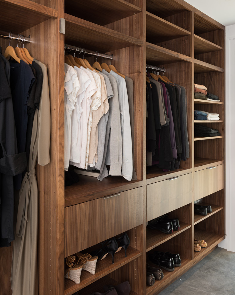 Diseño de armario vestidor unisex minimalista grande con armarios con paneles lisos, puertas de armario de madera oscura y suelo de cemento
