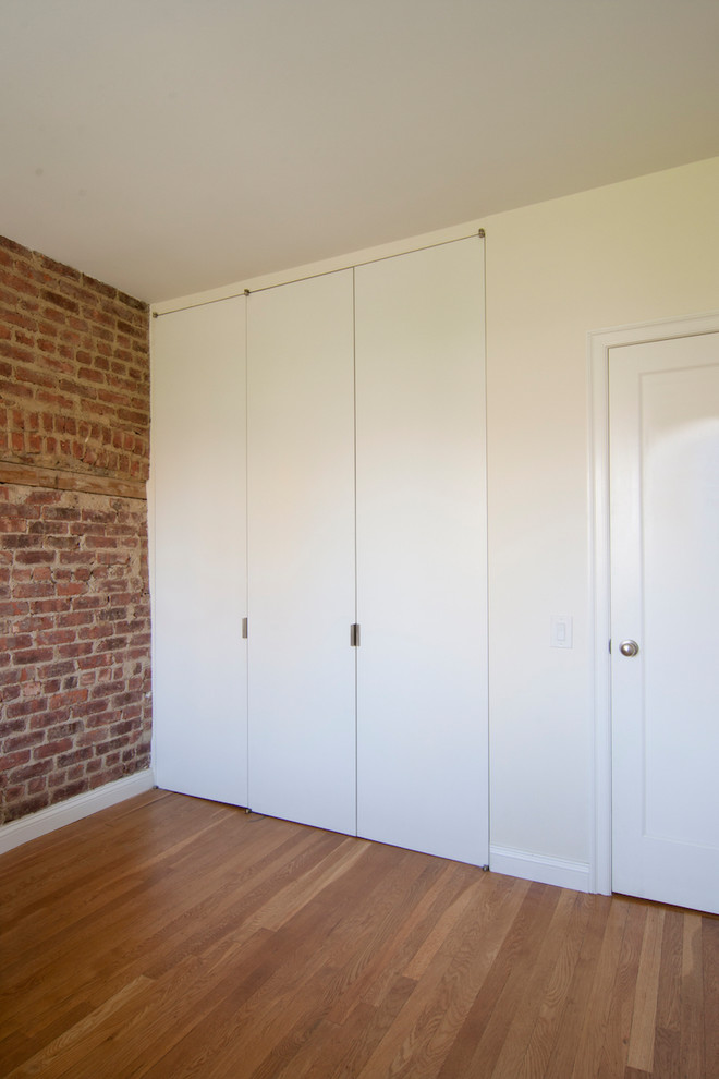 На фото: шкаф в нише среднего размера, унисекс в стиле лофт с плоскими фасадами, белыми фасадами, паркетным полом среднего тона и коричневым полом