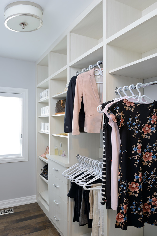 Modelo de vestidor de mujer clásico de tamaño medio con armarios con paneles lisos, puertas de armario blancas, suelo de madera en tonos medios y suelo marrón