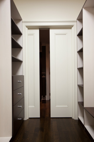 Modelo de armario vestidor unisex moderno grande con armarios con paneles lisos, puertas de armario de madera en tonos medios, suelo de madera oscura y suelo marrón