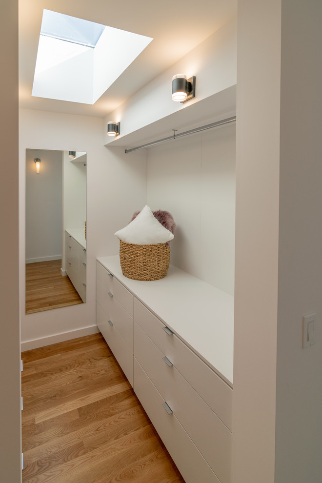 Ejemplo de armario vestidor unisex minimalista de tamaño medio con armarios con paneles lisos, puertas de armario blancas, suelo de madera en tonos medios y suelo marrón