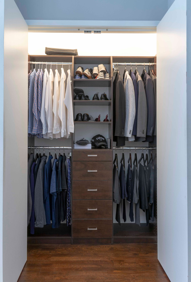Photo of a small contemporary gender neutral standard wardrobe in New York with flat-panel cabinets, dark wood cabinets, medium hardwood flooring and brown floors.