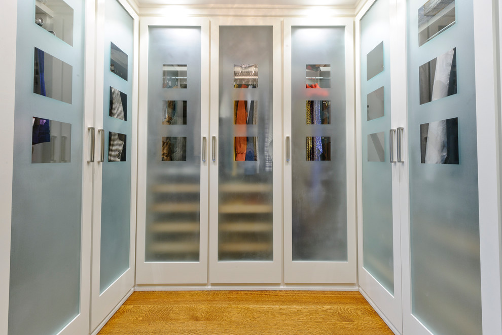 Inspiration for a timeless light wood floor walk-in closet remodel in Philadelphia with glass-front cabinets and white cabinets