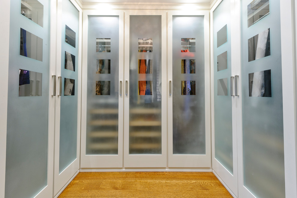 Ejemplo de armario vestidor clásico con armarios tipo vitrina, puertas de armario blancas y suelo de madera clara