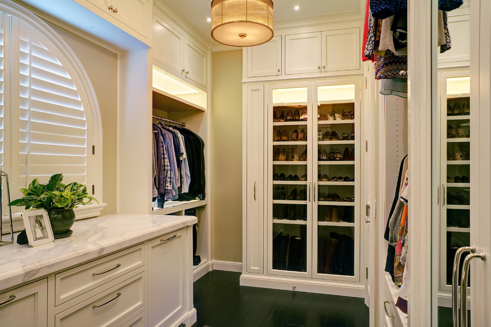 Imagen de vestidor unisex clásico renovado con armarios con paneles empotrados, puertas de armario blancas y suelo de madera oscura