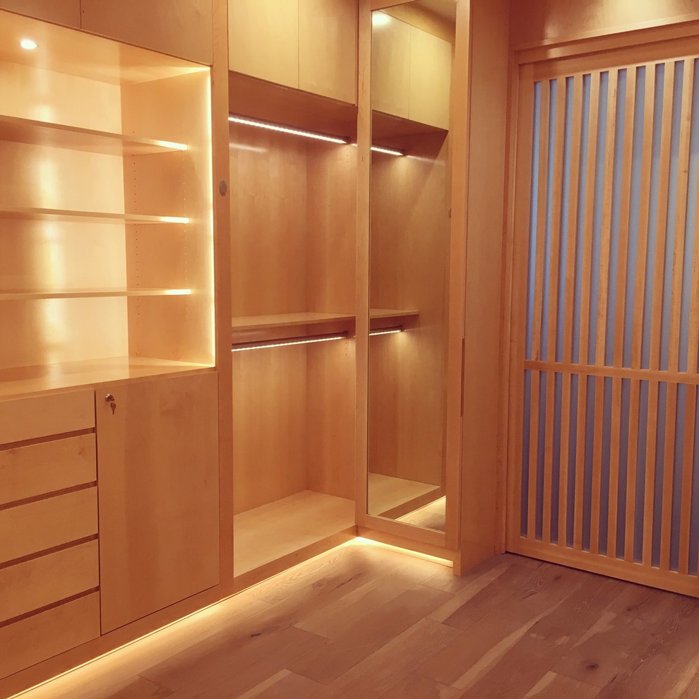 Immagine di un'ampia cabina armadio unisex minimal con ante lisce, ante in legno chiaro e parquet chiaro