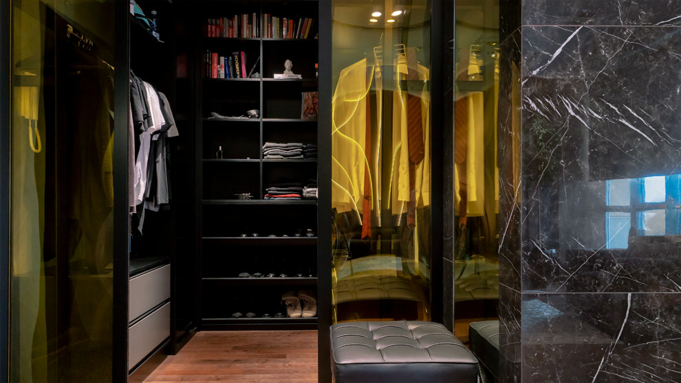 Ejemplo de vestidor unisex actual con armarios con paneles lisos, puertas de armario negras, suelo de madera en tonos medios y suelo marrón