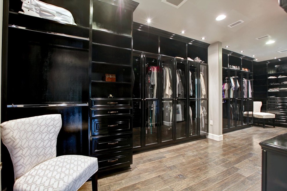 Ejemplo de armario vestidor unisex actual extra grande con armarios tipo vitrina, puertas de armario negras y suelo de madera en tonos medios