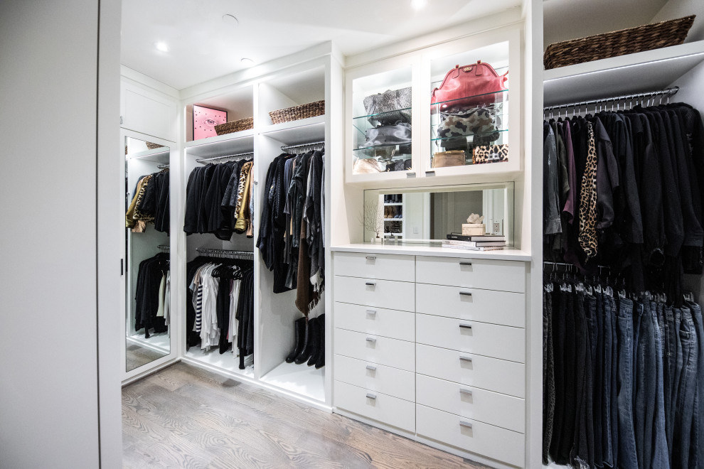 Imagen de armario vestidor unisex actual de tamaño medio con armarios con paneles lisos, puertas de armario blancas, suelo de madera en tonos medios y suelo marrón