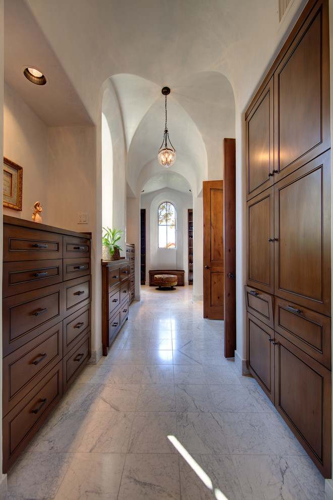 This is an example of a mediterranean wardrobe in Austin with dark wood cabinets and marble flooring.