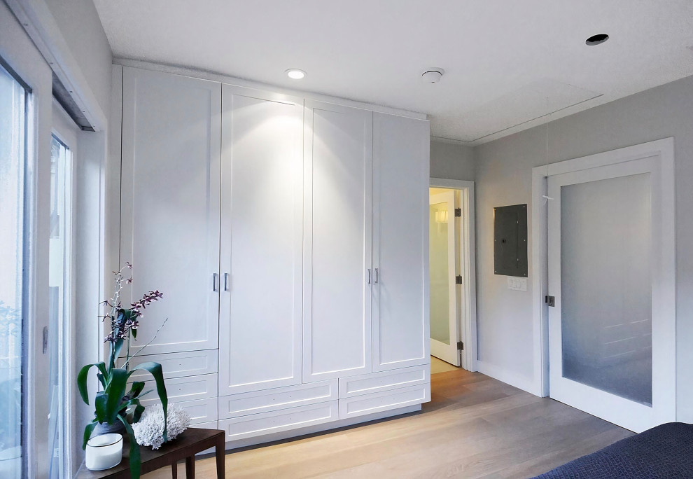 Cette photo montre une armoire encastrée bord de mer de taille moyenne et neutre avec un placard à porte shaker, des portes de placard blanches, parquet clair et un sol beige.