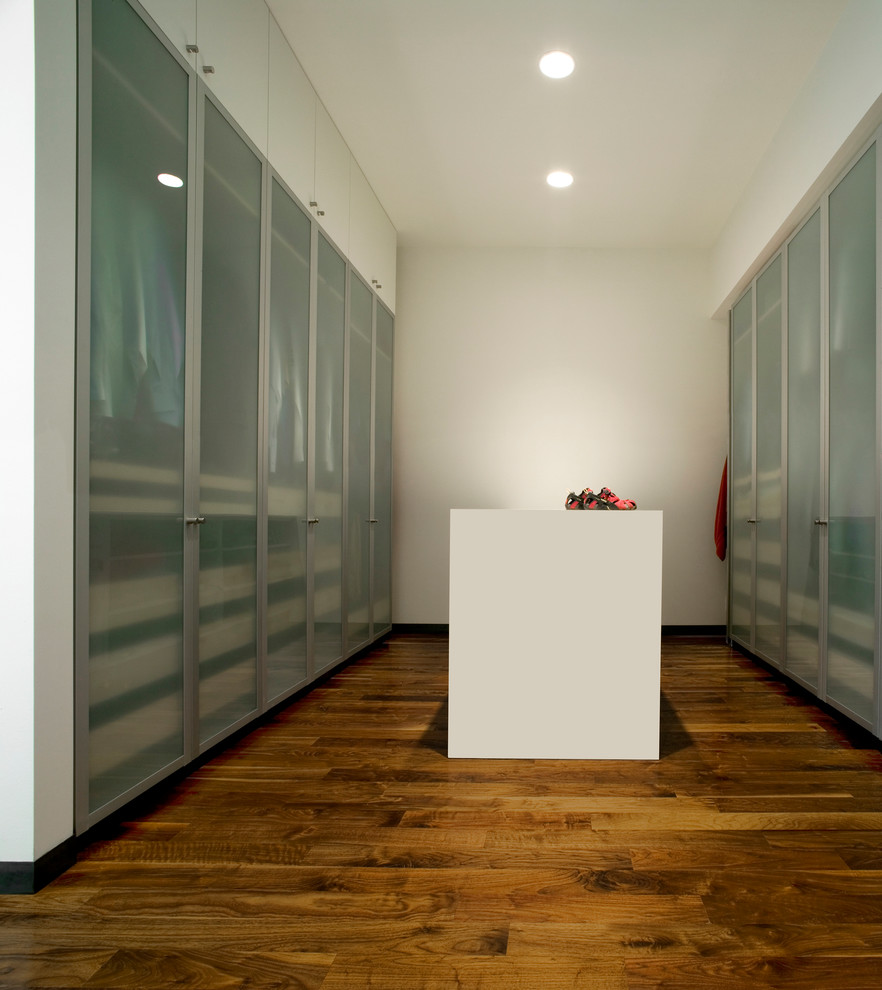 Immagine di una cabina armadio moderna con pavimento in legno massello medio e ante lisce