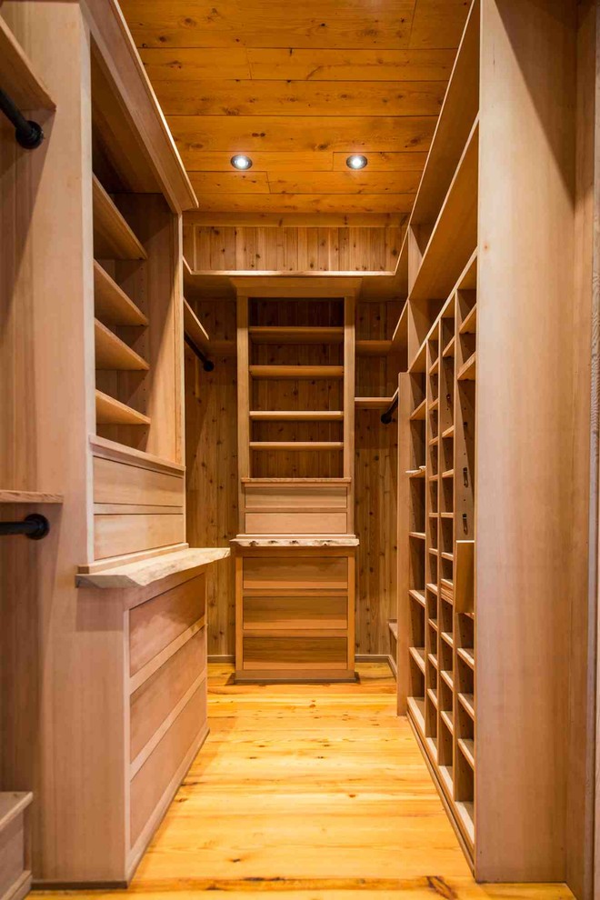 Modelo de armario vestidor unisex de estilo de casa de campo grande con armarios con paneles lisos, puertas de armario de madera oscura y suelo de madera clara