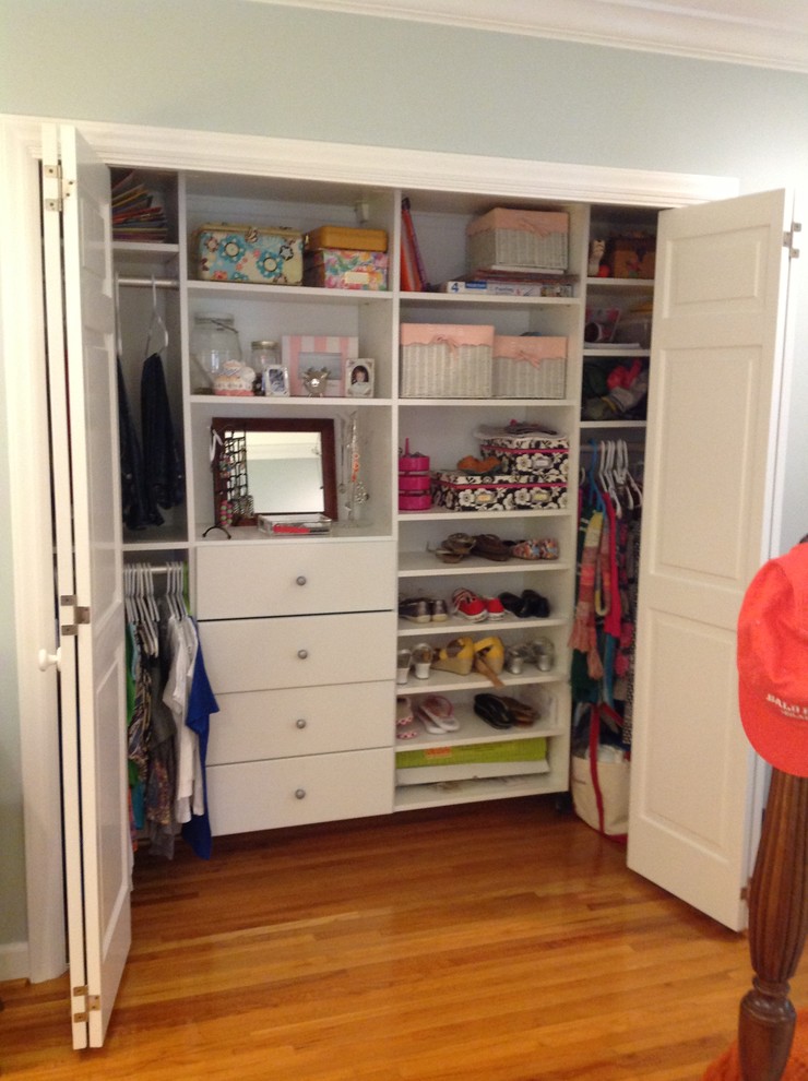 Modelo de armario unisex tradicional pequeño con armarios con paneles lisos, puertas de armario blancas, suelo de madera en tonos medios y suelo marrón