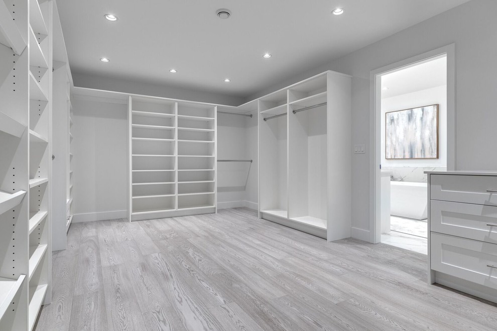 Modelo de armario vestidor unisex minimalista extra grande con armarios estilo shaker, puertas de armario blancas, suelo de madera clara y suelo gris