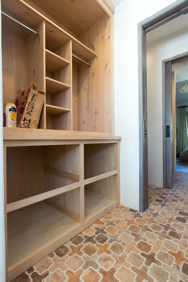 Imagen de armario vestidor unisex de estilo de casa de campo con puertas de armario de madera clara y suelo de baldosas de terracota