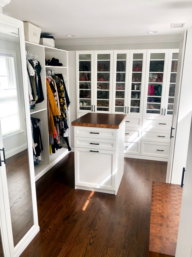 Diseño de armario vestidor unisex clásico de tamaño medio con armarios con paneles con relieve, puertas de armario blancas, suelo de madera oscura y suelo marrón