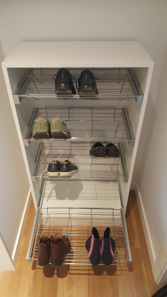 Imagen de armario unisex moderno pequeño con armarios con paneles lisos, puertas de armario blancas, suelo laminado y suelo marrón