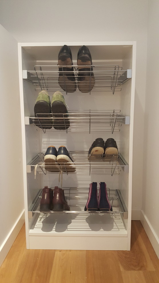 Imagen de armario unisex minimalista pequeño con armarios con paneles lisos, puertas de armario blancas, suelo laminado y suelo marrón