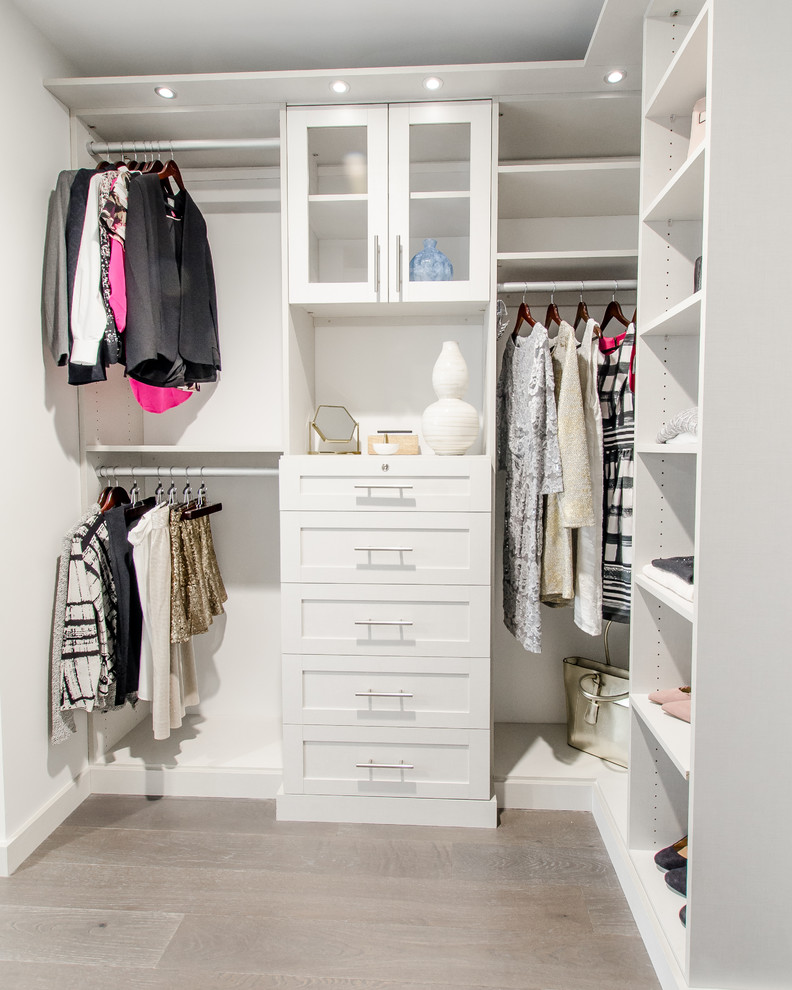 Imagen de armario vestidor unisex minimalista grande con puertas de armario blancas y suelo de madera en tonos medios