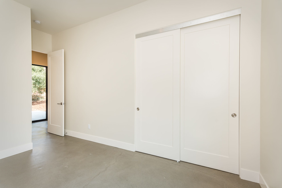 На фото: шкаф в нише среднего размера, унисекс в стиле модернизм с фасадами в стиле шейкер, белыми фасадами и бетонным полом с