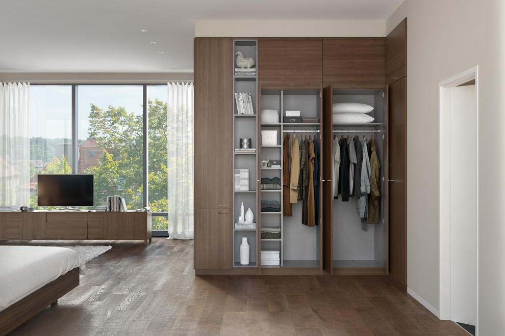Modelo de armario unisex moderno de tamaño medio con puertas de armario de madera oscura, suelo de madera en tonos medios y armarios con paneles lisos