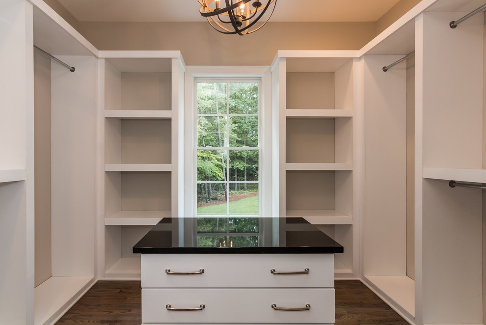 This is an example of a large rural gender neutral walk-in wardrobe in Raleigh with flat-panel cabinets, white cabinets and medium hardwood flooring.