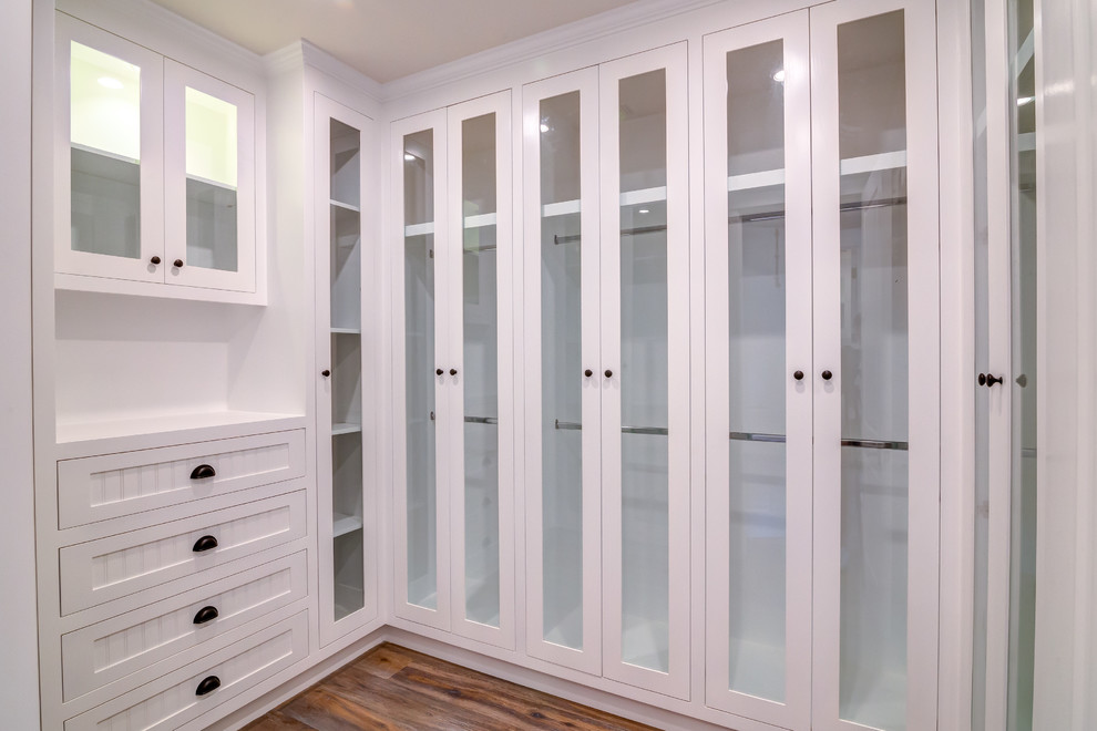 Klassisk inredning av ett litet walk-in-closet för könsneutrala, med luckor med glaspanel, vita skåp, laminatgolv och brunt golv