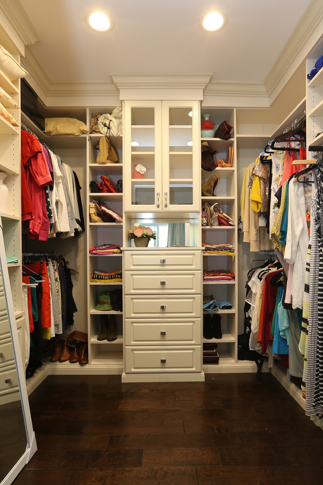 Modelo de armario vestidor de mujer moderno de tamaño medio con puertas de armario blancas, suelo de madera oscura y armarios con paneles con relieve