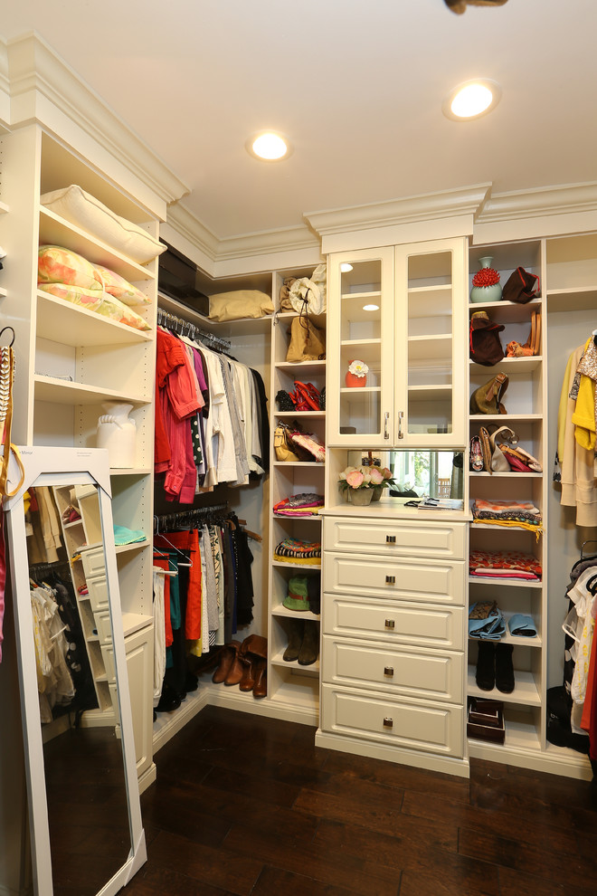 Imagen de armario vestidor de mujer minimalista de tamaño medio con puertas de armario blancas, suelo de madera oscura y armarios con paneles con relieve