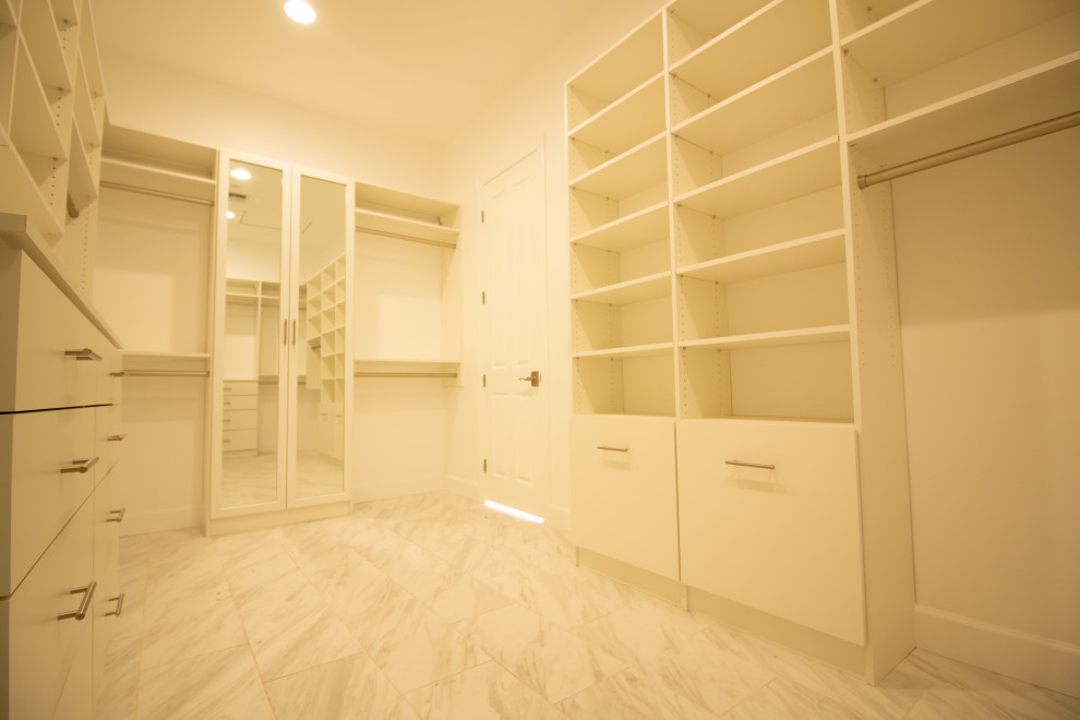 Ejemplo de armario vestidor unisex actual grande con armarios con paneles lisos, puertas de armario blancas, suelo de mármol y suelo gris