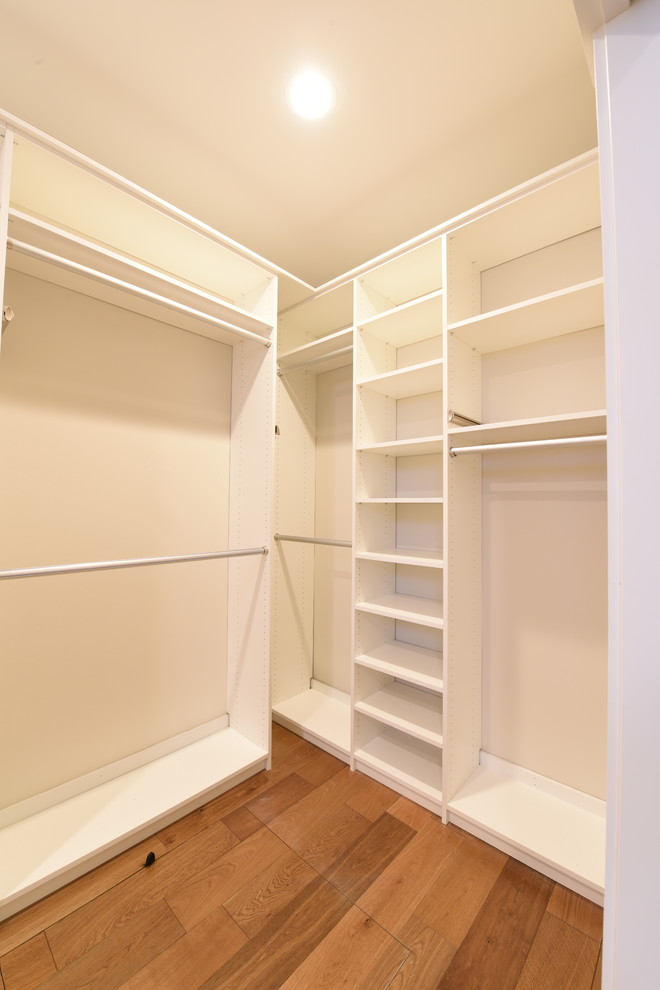 This is an example of a medium sized contemporary gender neutral walk-in wardrobe in Other with medium hardwood flooring and brown floors.