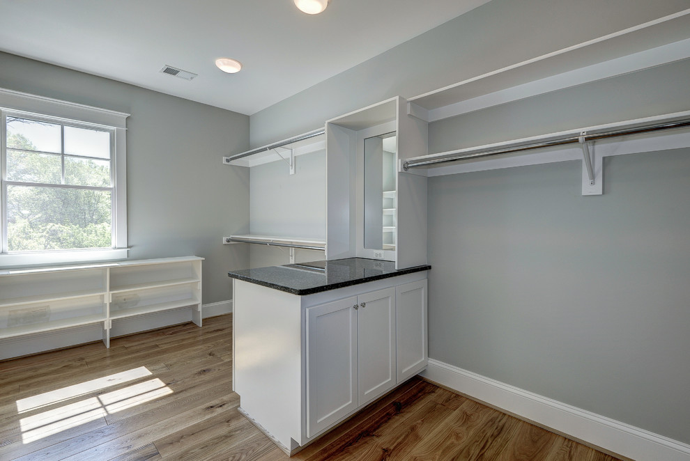 Inspiration for an expansive modern gender neutral walk-in wardrobe in DC Metro with raised-panel cabinets, white cabinets and light hardwood flooring.