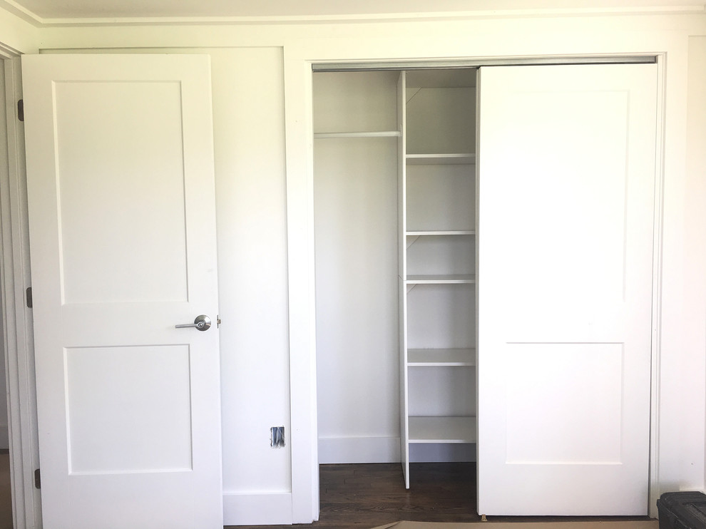 Cette photo montre un placard dressing tendance de taille moyenne et neutre avec un placard avec porte à panneau encastré, des portes de placard blanches et un sol en bois brun.