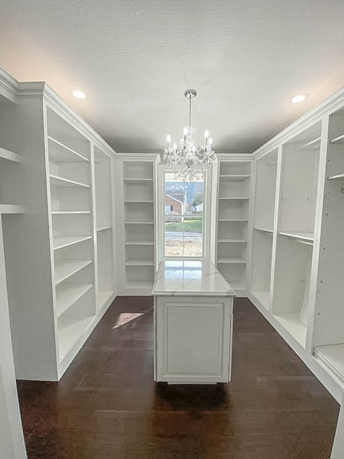 Inspiration for a large traditional gender neutral walk-in wardrobe in Huntington with raised-panel cabinets, white cabinets, dark hardwood flooring and brown floors.