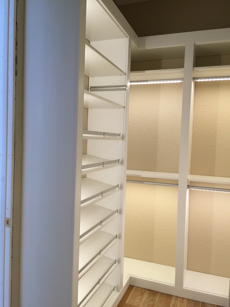 Modelo de armario vestidor unisex clásico renovado con armarios con paneles lisos, suelo de madera en tonos medios y puertas de armario blancas