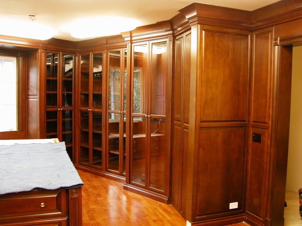Foto de armario vestidor unisex clásico extra grande con armarios con paneles con relieve, puertas de armario de madera oscura, suelo de madera en tonos medios y suelo marrón