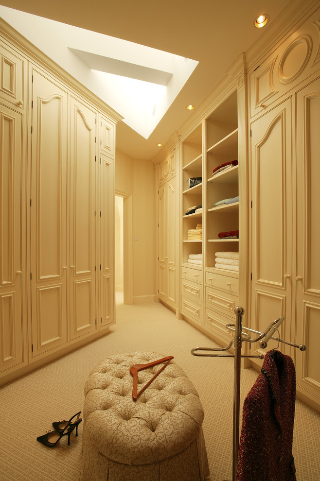 Cette image montre un dressing room traditionnel avec un placard avec porte à panneau encastré et des portes de placard beiges.