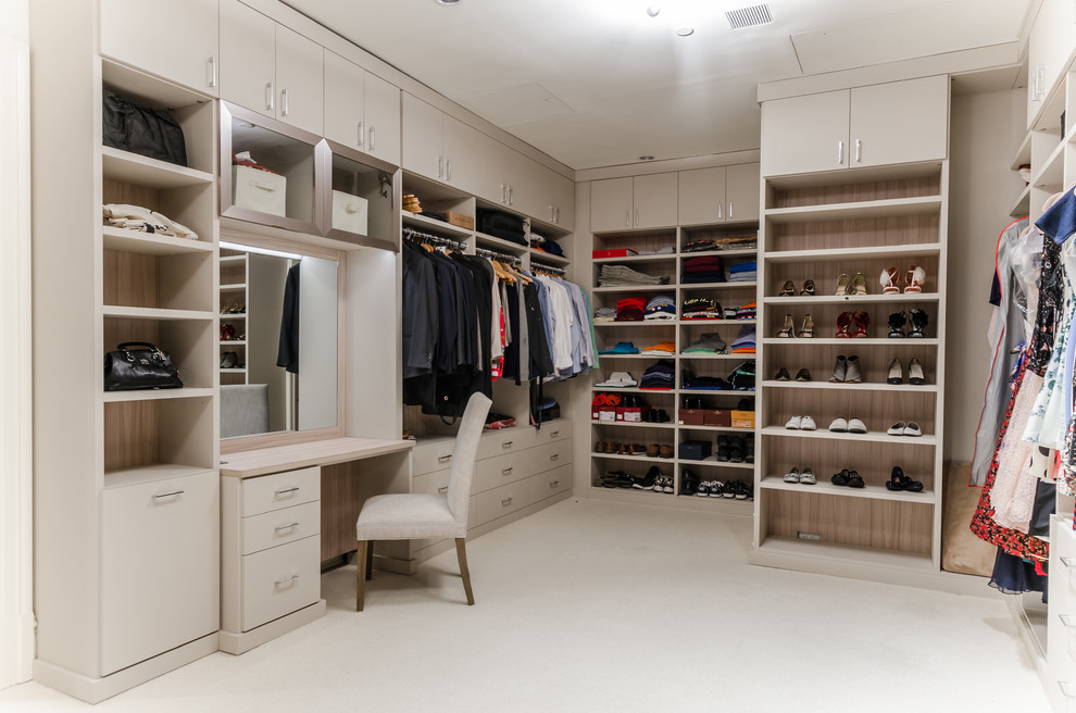 Photo of a modern gender neutral walk-in wardrobe in New York with open cabinets, beige cabinets, carpet and beige floors.